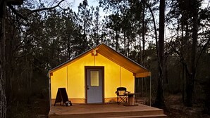 Eine kleine, eingeschossige Holzhütte mit einer Haustür, einer kleinen Veranda und einem Stuhl.