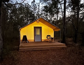 Une petite cabane à un seul étage, avec une porte d’entrée, un petit porche et une chaise.