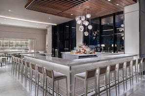 A modern bar area with a central island, bar stools, and a unique chandelier. - AC Hotel Kingston Jamaica (Kingston)