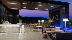 Uma área de estar ao ar livre moderna, com banquetas de bar, mesas e piscina.