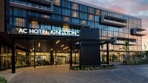 Um hotel moderno com fachada de vidro, entrada coberta e uma placa com a inscrição 'AC HOTEL KINGSTON'.