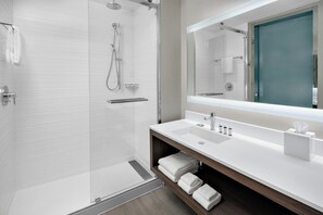 A modern bathroom with a glass shower enclosure, a white sink, a mirror, and a wooden vanity. - AC Hotel Kingston Jamaica (Kingston)