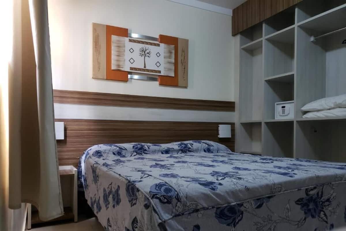 Quarto com cama, guarda-roupa e telefone fixado na parede.