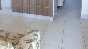 Ein Zimmer mit einem flachbildfernseher, der an einer Wand aus Holzpaneelen befestigt ist, einer gemusterten Couch und einem Blick in einen Flur mit einem Vorhang.