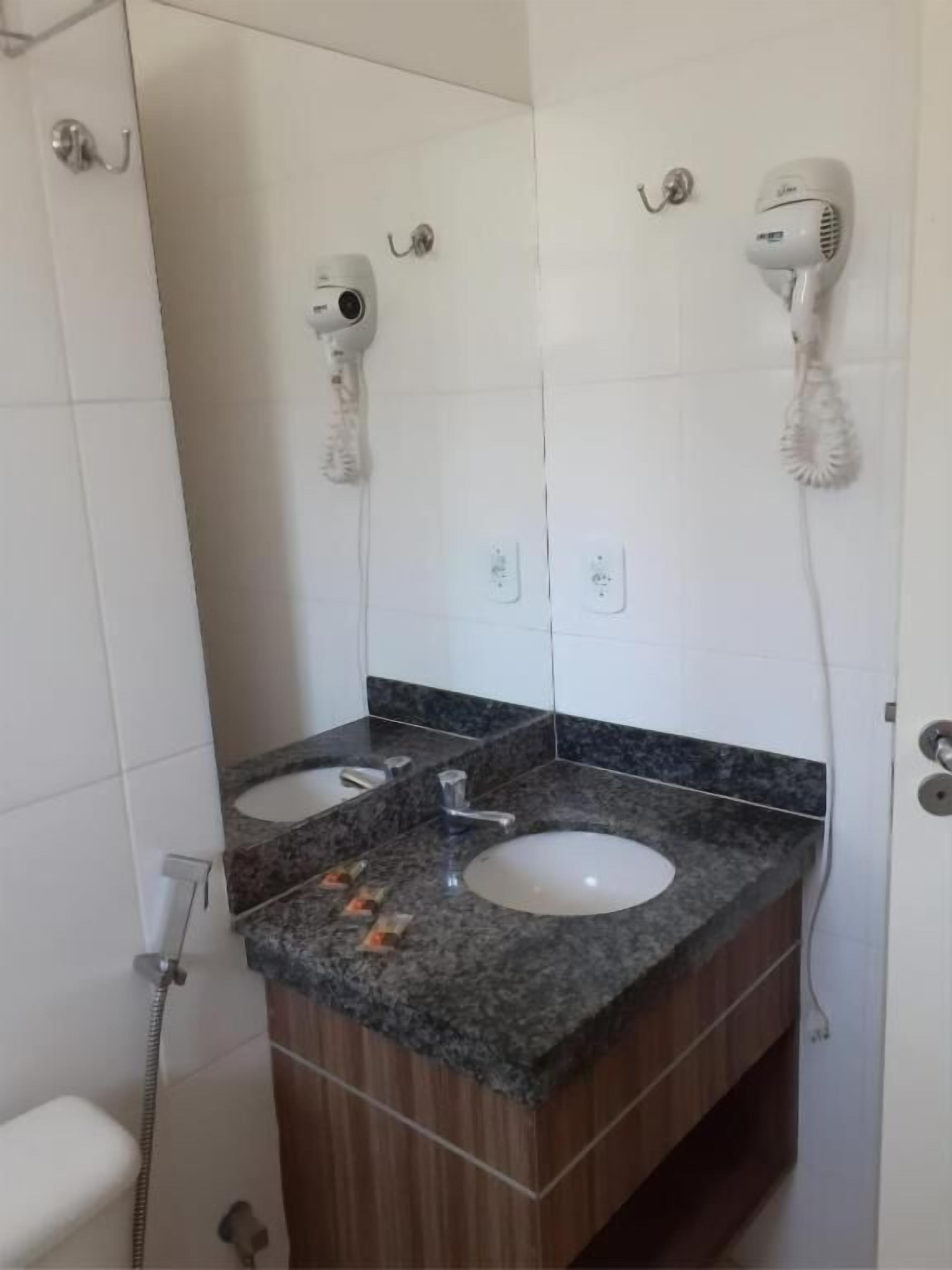 A bathroom with two sinks, a mirror, and two hair dryers mounted on the wall.