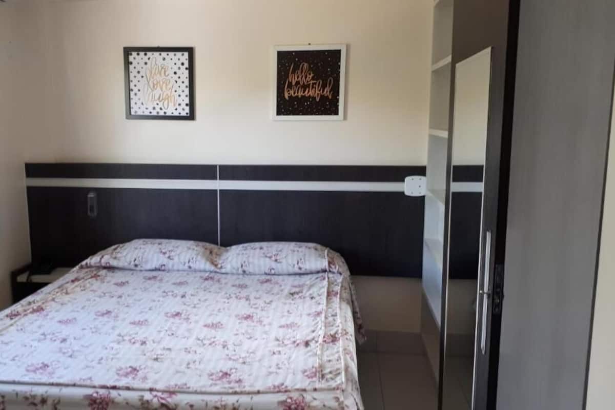 Quarto com uma cama, duas fotos emolduradas na parede, um guarda-roupa e uma porta.