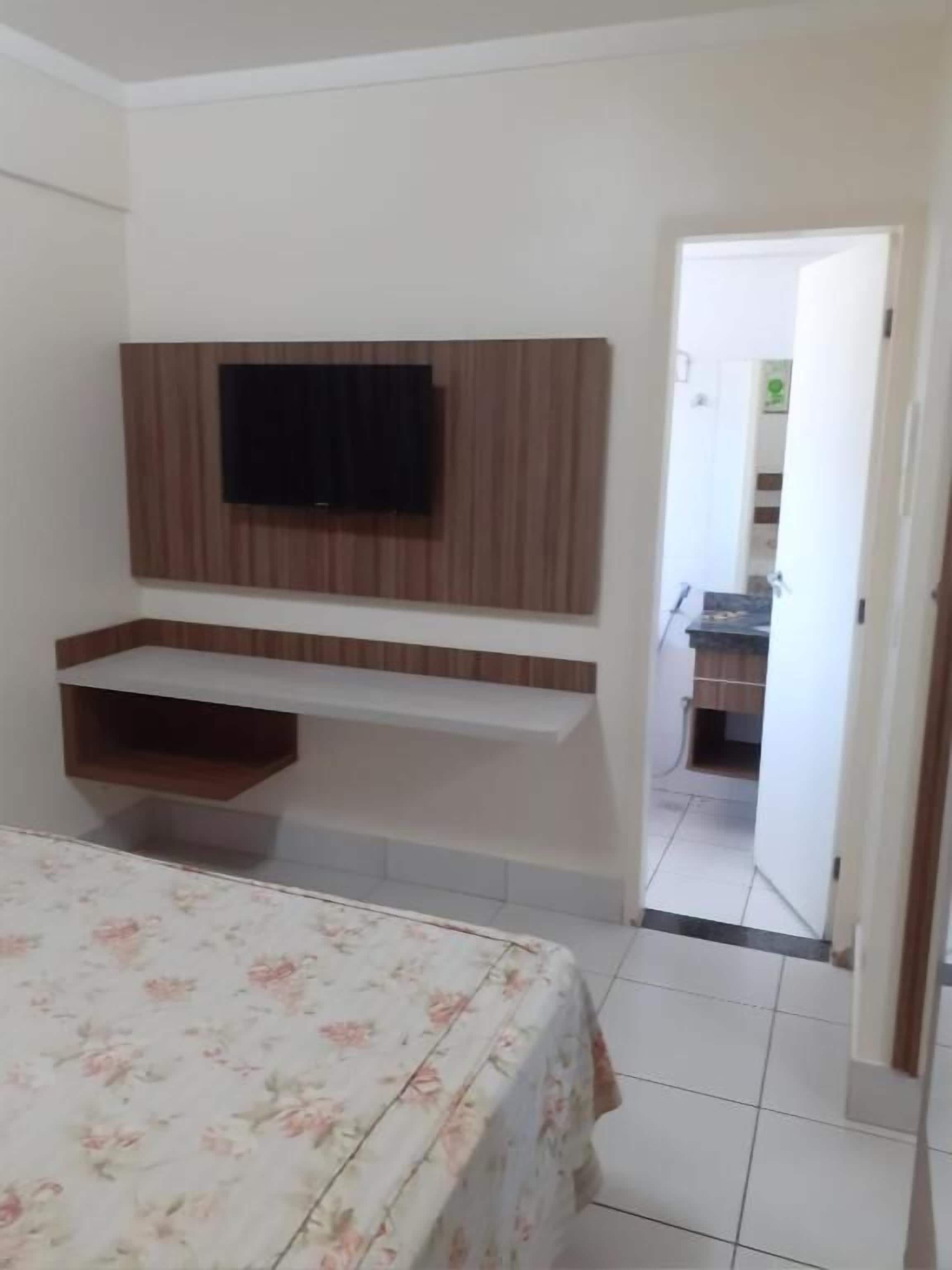 A bedroom with a bed, a TV mounted on the wall, and a small desk area.