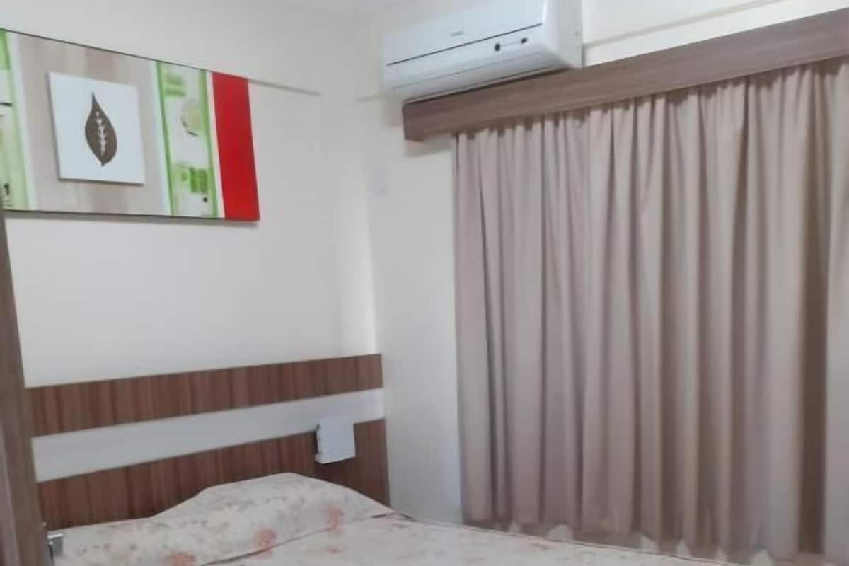 Um quarto com uma cama, ar condicionado, janela com cortinas e parede com quadros.