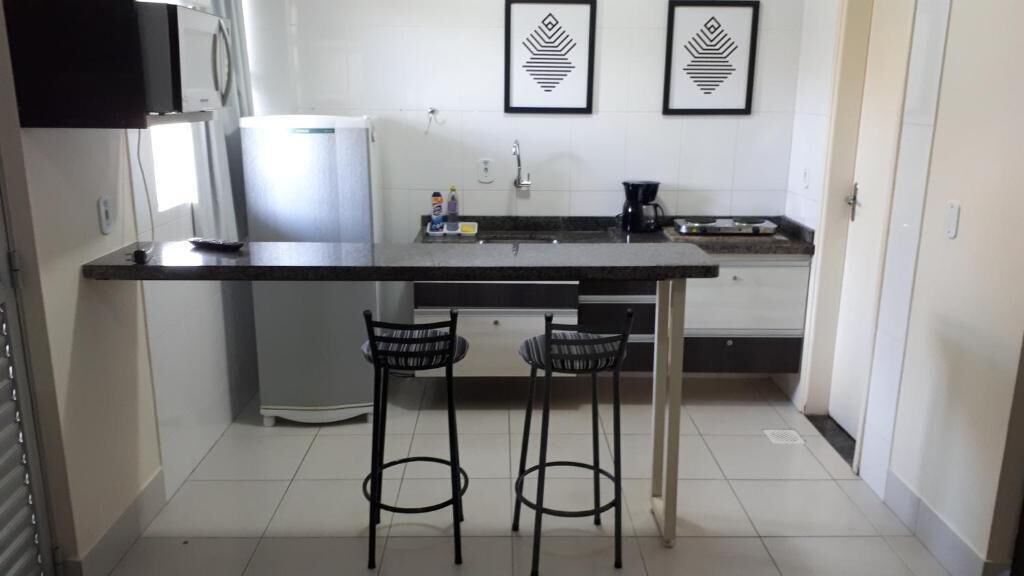 A kitchen with a black countertop, two bar stools, a refrigerator, and two framed wall art pieces.