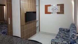 Ein Zimmer mit einem an einer Holzkommode befestigten Fernseher, einer gemusterten Couch und einem an der Wand hängenden Kunstwerk.