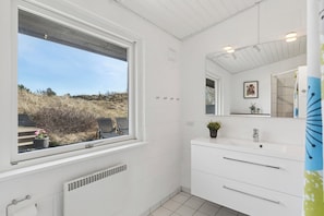 A bathroom with a large window, white tiles, a sink, and a mirror. - Spacious holiday home 150 m from the beach (Ålbæk)