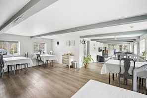 A spacious dining area with multiple tables and chairs, a wooden floor, and a view of the outside.