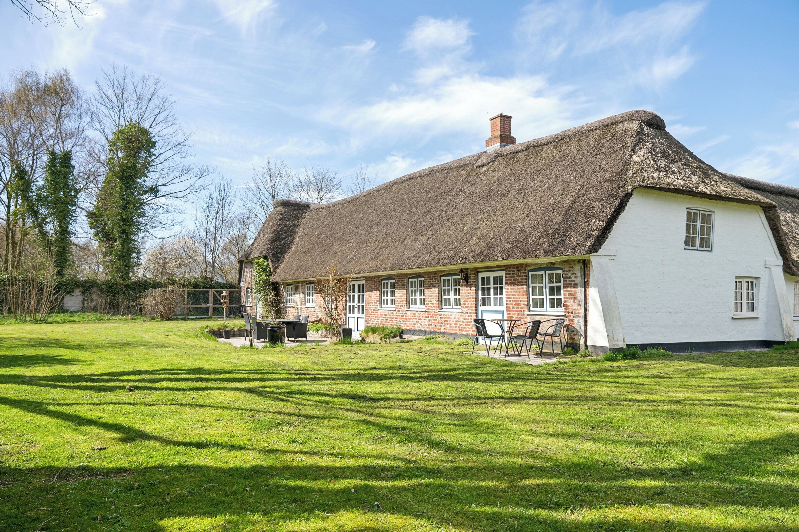 A traditional thatched-roof house with a white exterior, a well-maintained lawn, and a clear sky.