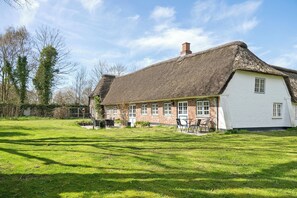 A traditional thatched-roof house with a white exterior, a well-maintained lawn, and a clear sky.