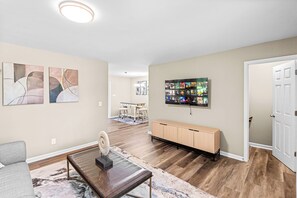 A living room with a sofa, coffee table, artwork, a TV wall mount, and a wooden cabinet. - Large Home/ Fully Appointed /Game Room! (Mableton)