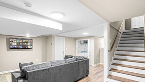 Ein modernes Wohnzimmer mit einem Ecksofa, einer Treppe und einer an der Wand befestigten Unterhaltungseinrichtung.