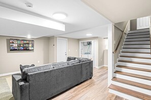 A modern living room with a sectional sofa, a staircase, and a wall-mounted entertainment unit. - Large Home/ Fully Appointed /Game Room! (Mableton)