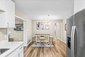 A kitchen with a white countertop, a stainless steel refrigerator, a dining table with stools, and a chandelier. - Large Home/ Fully Appointed /Game Room! (Mableton)