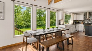 Eine moderne Küche mit großen Fenstern, ein Essbereich mit Holztisch und -stühlen und Blick auf einen grünen Garten.