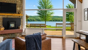 Ein Zimmer mit Kamin aus Stein, einem großen Fenster mit Seeblick, einer Holzterrasse davor und einer Bank.