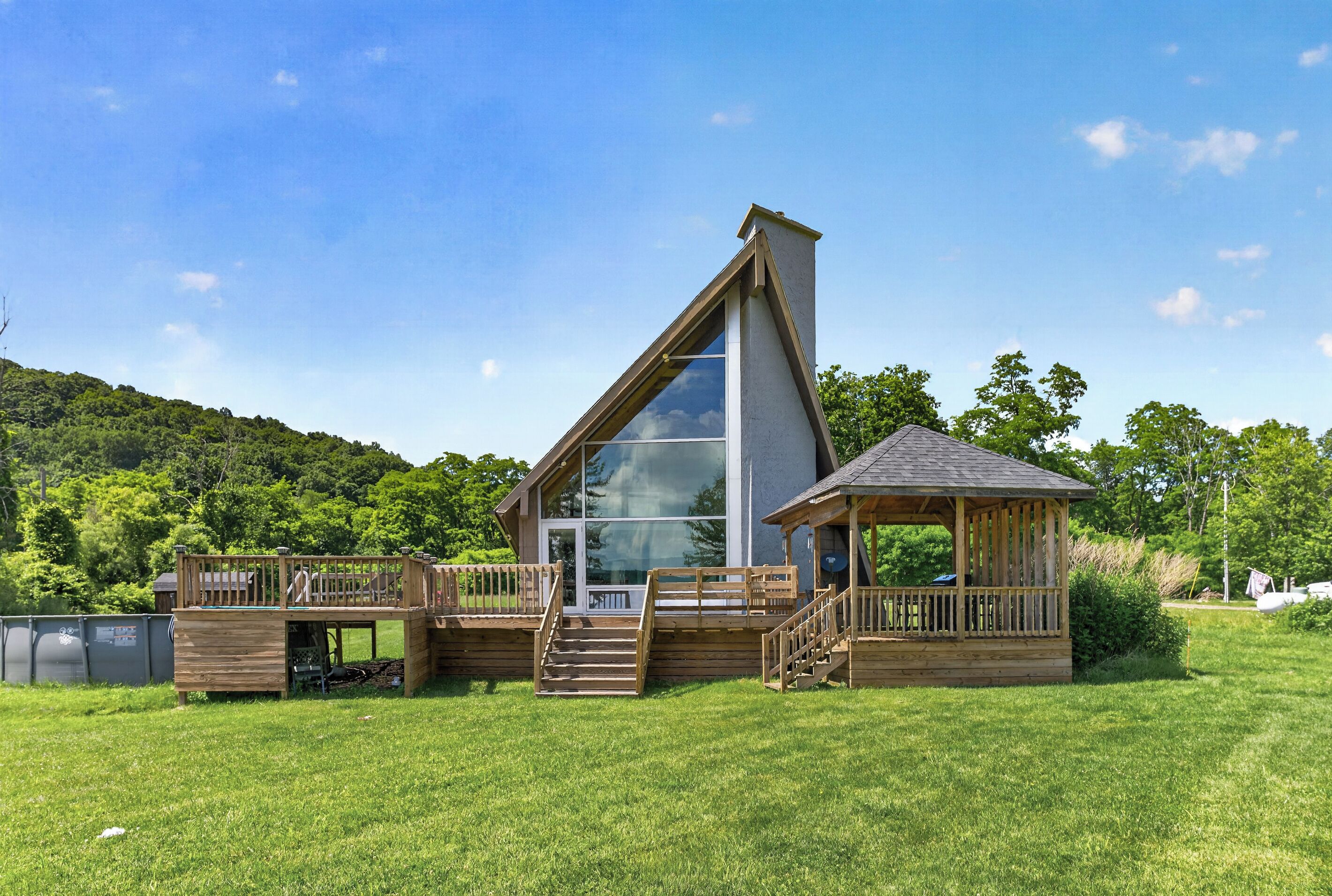 Une maison moderne dotée d’une grande baie vitrée, d’une terrasse en bois et d’un petit kiosque.