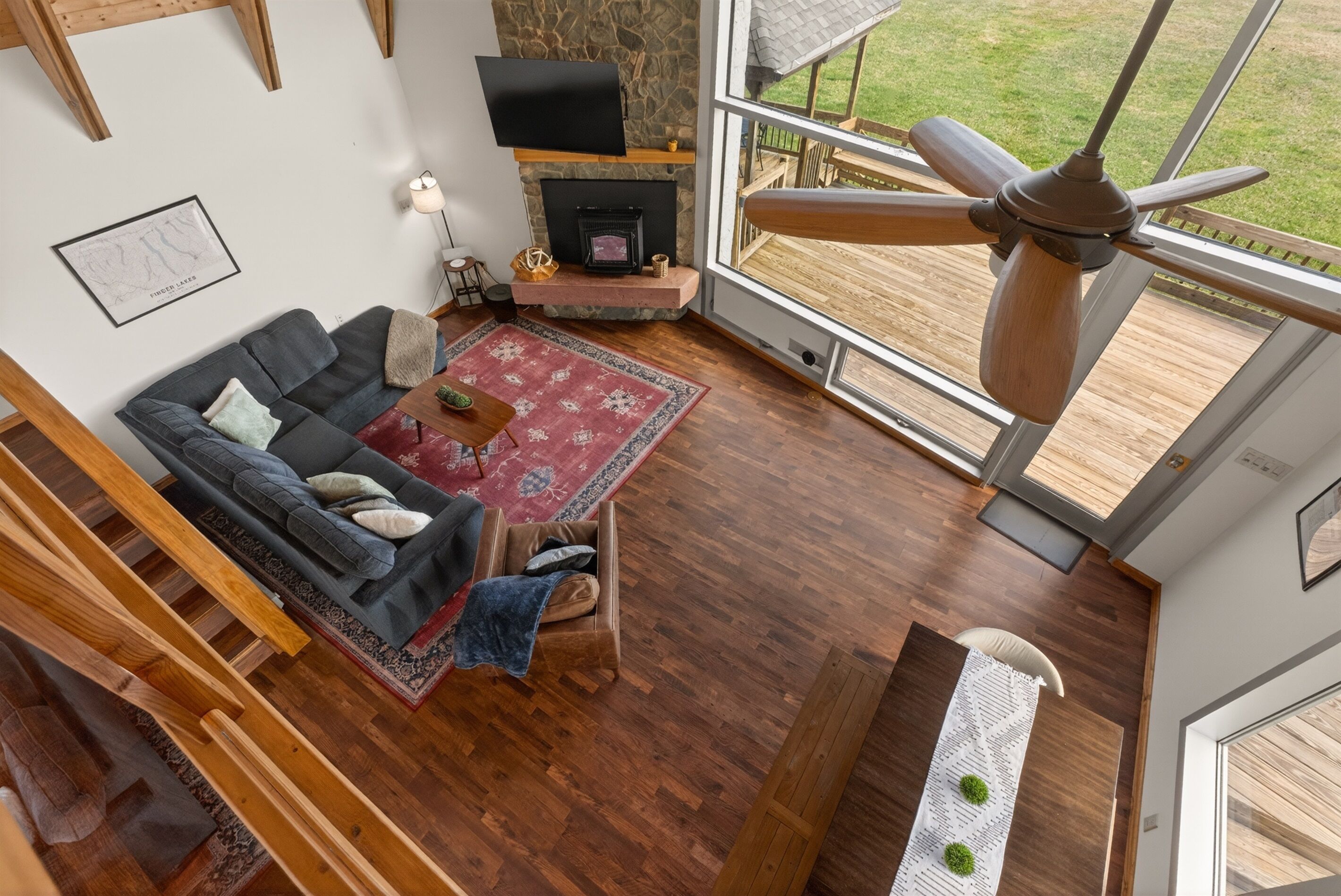 A modern living room with a fireplace, a ceiling fan, a large window, and a wooden floor.