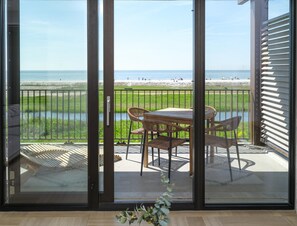 A balcony with a table and chairs, a view of the beach, and a railing.