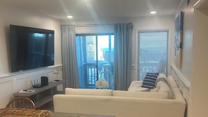 En moderne stue med et fladskærms-tv, en sofa, et spisebord med stole og en balkon med udsigt.