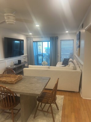 Un salon moderne doté d’un téléviseur à écran plat, d’un canapé, d’une table à manger avec des chaises et d’un balcon offrant une vue agréable.