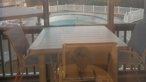 Spiseområde ved poolen med udsigt over havet og en bygning i baggrunden.