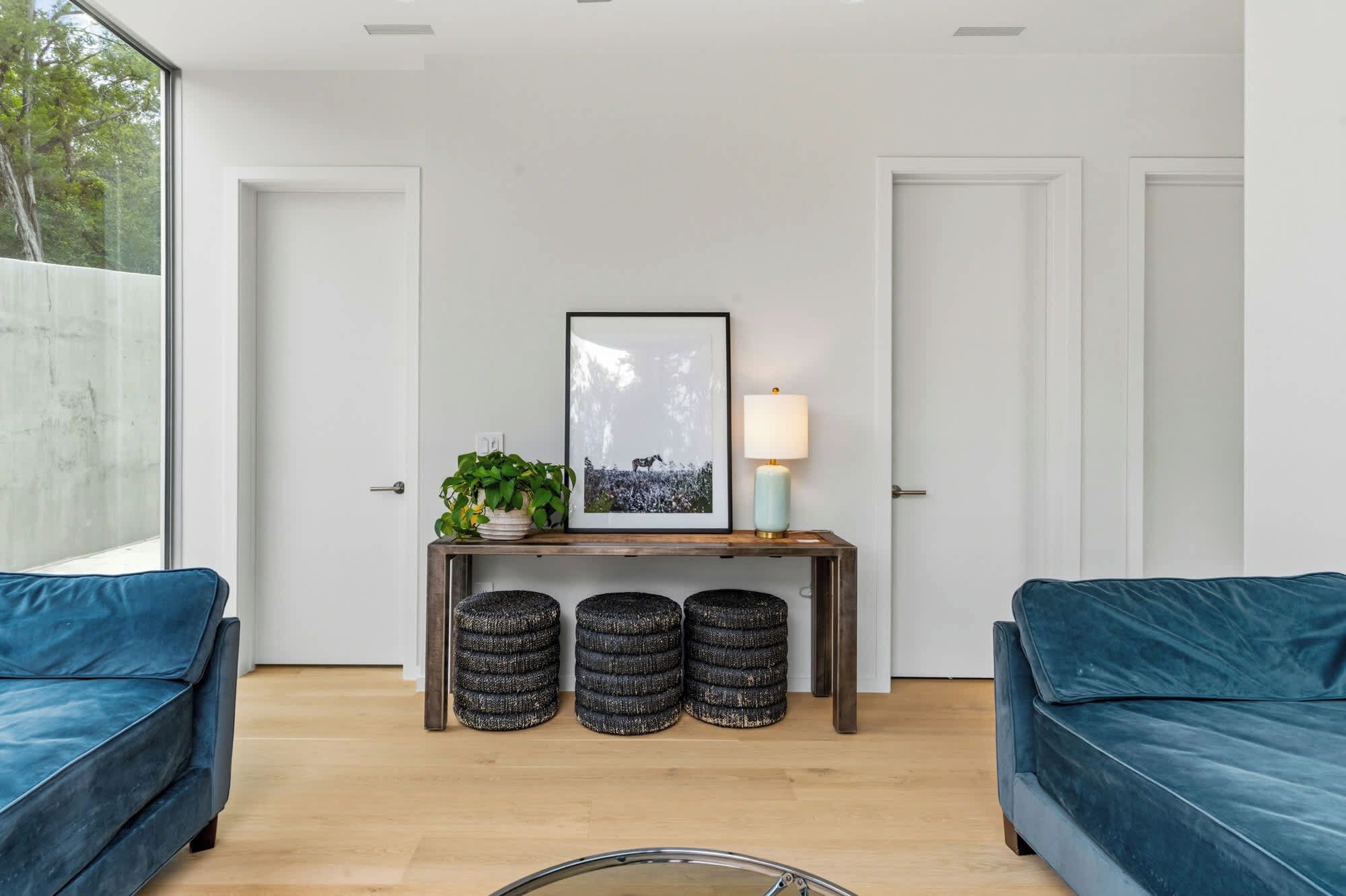 Un salon moderne avec un canapé bleu, une console en bois sur laquelle est posée une photo encadrée, une lampe et deux tabourets ronds.
