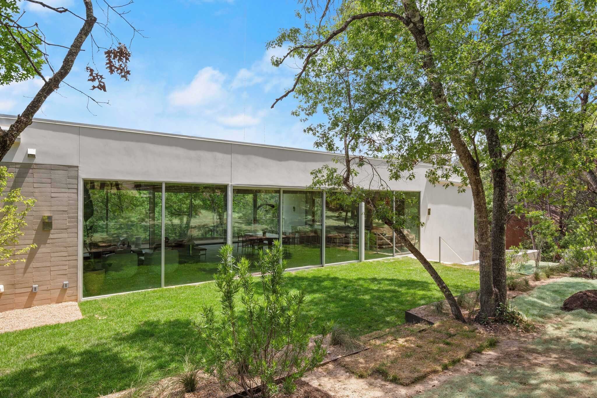 A modern building with large glass windows, a brick wall, and a well-maintained lawn.