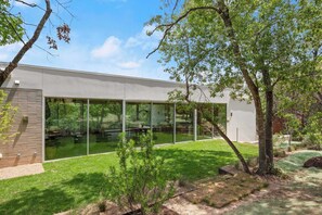 A modern building with large glass windows, a brick wall, and a well-maintained lawn. - Thanksgiving in Austin | Chef’s Kitchen + Hot Tub (West Lake Hills)