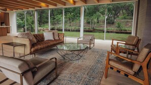 A modern living room with a glass coffee table, leather sofas, and wooden chairs.