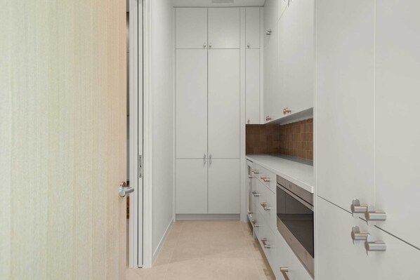 A narrow hallway with white cabinets, a wooden door, and a tiled floor. - Thanksgiving in Austin | Chef’s Kitchen + Hot Tub (West Lake Hills)