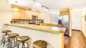 A kitchen with a central island, bar stools, a refrigerator, and a microwave. - 2BR Oyhut Bay Condo | Fireplace | Private Deck (Ocean Shores)