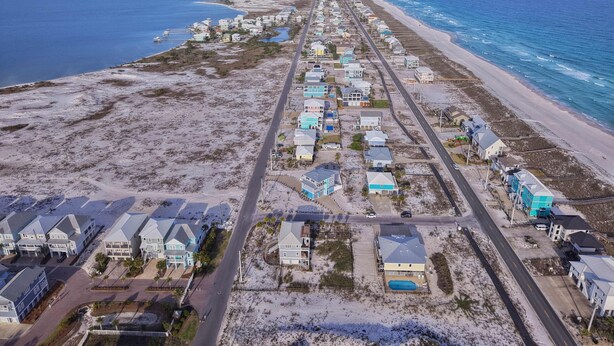Vue aérienne d’une zone résidentielle côtière, avec des maisons, des routes et une plage.