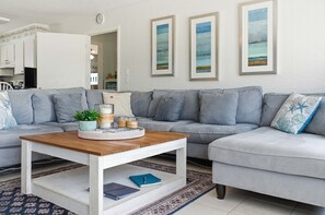 A living room with a grey sofa, a wooden coffee table, and framed artwork on the wall. - Steps to the Beach • Gulf + Sound Views (Navarre Beach)