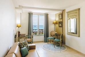 Una habitación con sofá, una mesa de comedor con sillas, ventana con cortinas, una lámpara y un espejo en la pared.
