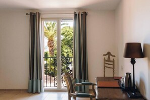 Quarto com porta de vidro deslizante para uma varanda, uma cadeira de madeira, uma mesa pequena e um abajur.