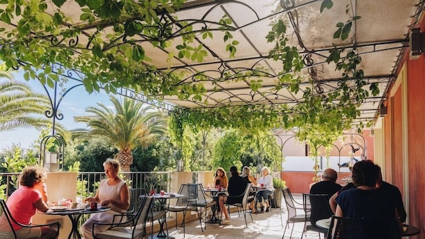 An outdoor café with tables and chairs, surrounded by greenery and a metal pergola structure. - Boutique Hotel Liberata (L'Île-Rousse)