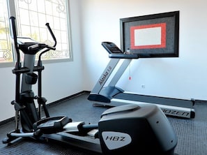 Un gimnasio en casa con una bicicleta estática, una cinta de correr y una máquina de remo.