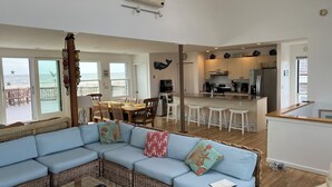 Ein Wohnzimmer mit blauem Sofa, eine Essecke mit Tisch und Stühlen, eine Küche mit Kühlschrank und Herd sowie ein Balkon mit Meerblick.
