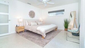 Une chambre à coucher comprenant un lit, des tables de chevet, un ventilateur de plafond, une fenêtre, un miroir et une plante en pot.
