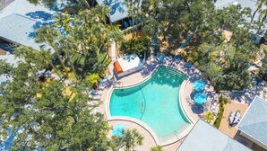 Vue aérienne d’un complexe hôtelier avec une piscine, des chaises longues et des palmiers.