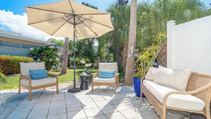 Une terrasse extérieure avec deux fauteuils en osier, un canapé, un grand parasol et une plante en pot.