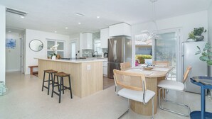Une cuisine moderne dotée d’un îlot central, de tabourets de bar, d’une table à manger avec des chaises et d’un réfrigérateur.
