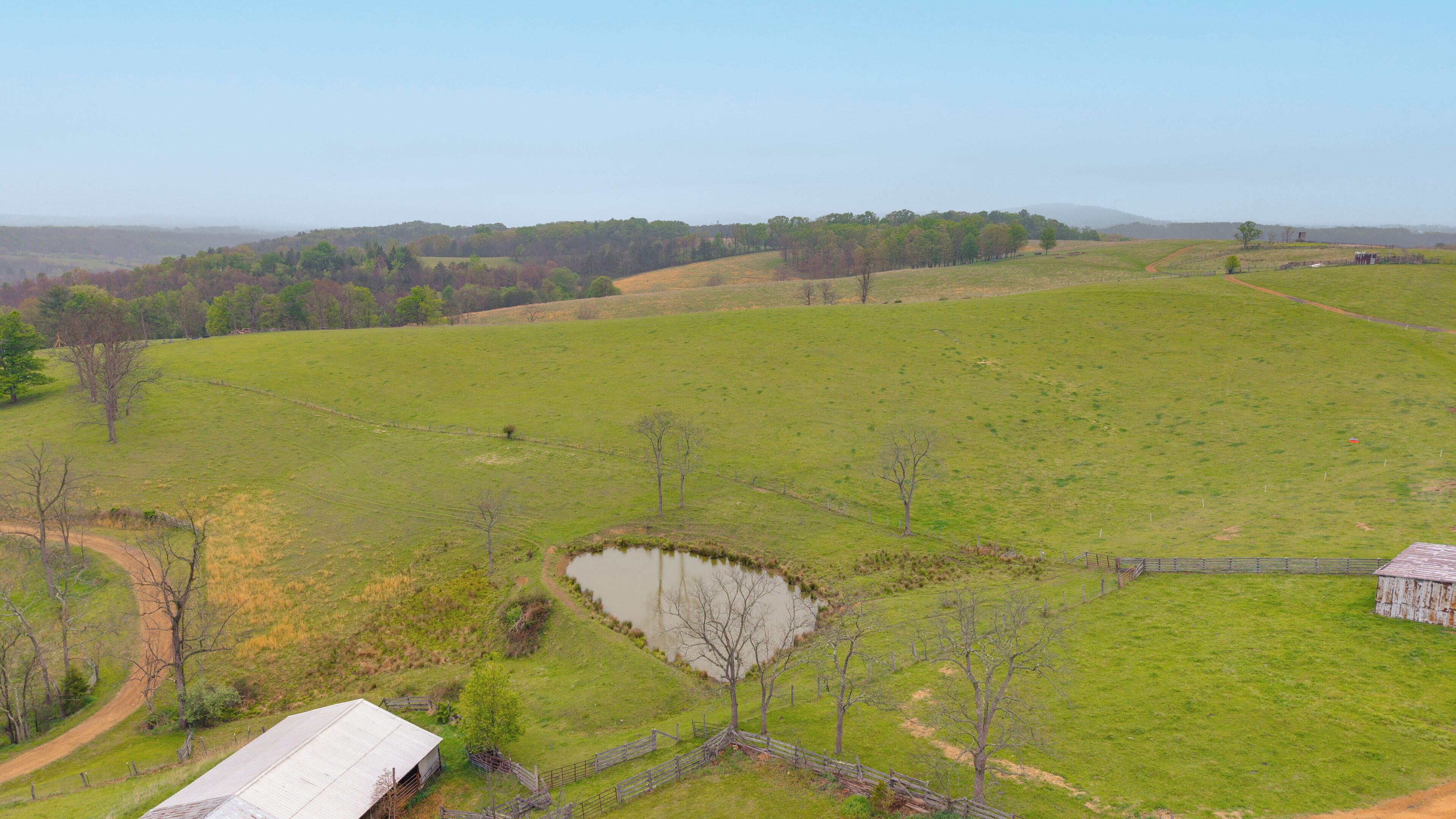 A rural landscape with a pond, a fenced area, and a building with a metal roof.