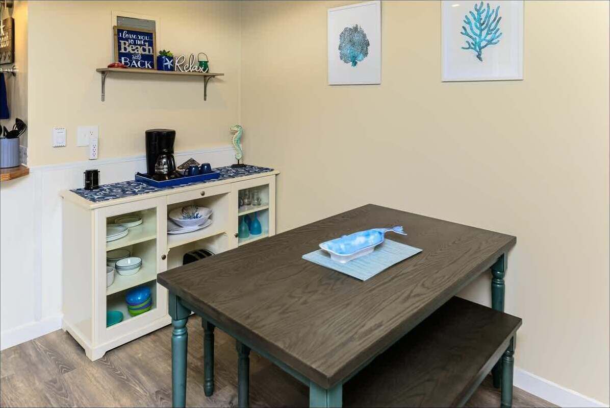 A kitchen with a wooden table, a coffee maker, and a shelf with dishes.