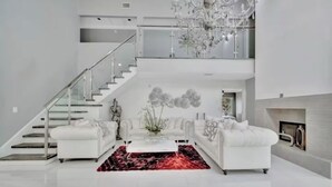 A modern living room with a staircase, white sofas, a glass coffee table, and a chandelier. - Welcome to your Private Tampa escape — designed for unforgettable group stays! (Tampa)